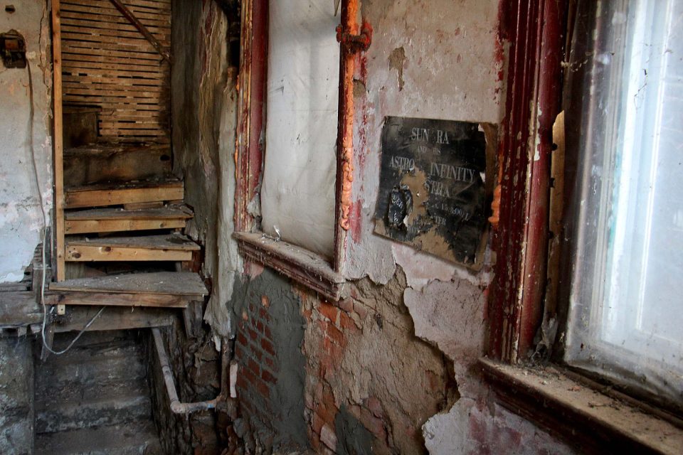partially collapsed interior of old house with torn and faded vintage Sun Ra concert poster on crumbling wall
